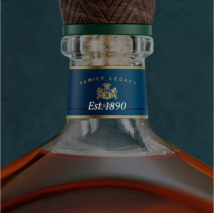 Close-up of a whiskey or cognac bottle neck with a blue label reading 'FAMILY LEGACY Est.1890' and gold detailing, topped with a dark green and brown stopper against a dark teal background.