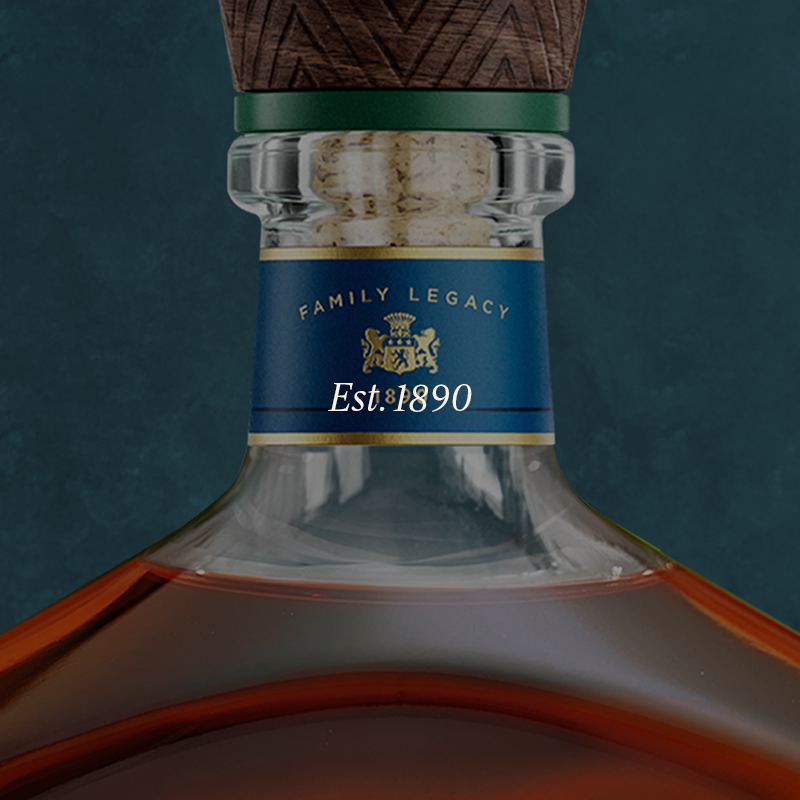 Close-up of a whiskey or cognac bottle neck with amber liquid, a dark green band, a cork stopper, and a blue label reading "FAMILY LEGACY" and "Est. 1890" against a dark teal background.