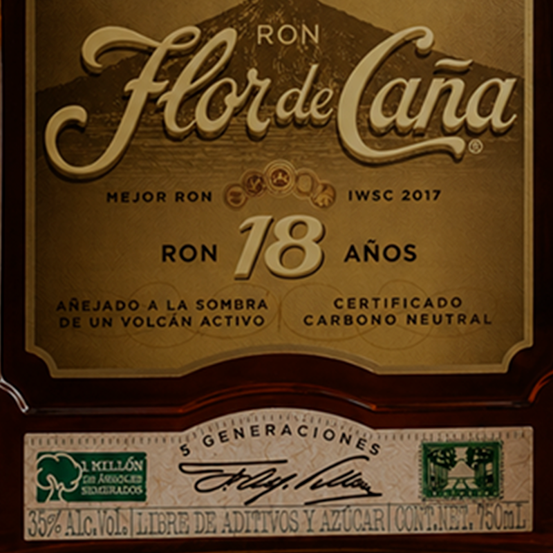 Close-up of a Ron Flor de Cana 18-year-old rum bottle label, showing the brand name in elegant gold lettering on a dark brown background with additional Spanish text and certification details.