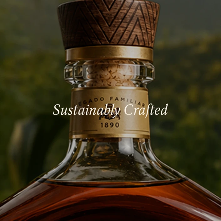 Close-up of a glass bottle with amber liquid, a gold neck label reading 1890, a textured dark wood stopper, and the text 'Sustainably Crafted' overlaid across the center.